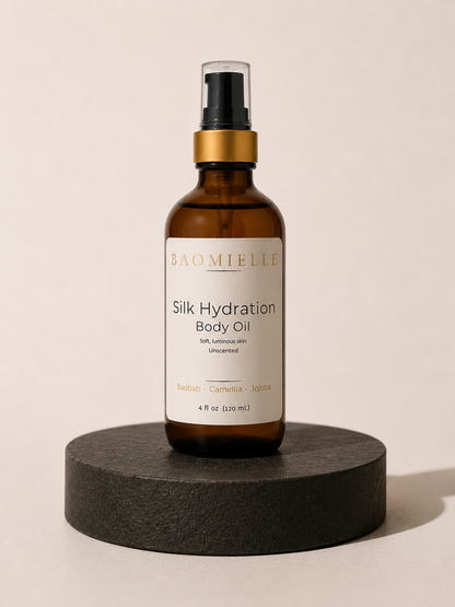 Bottle of Baomielle Silk Hydration Body Oil on a neutral pedestal with minimal editorial lighting.
